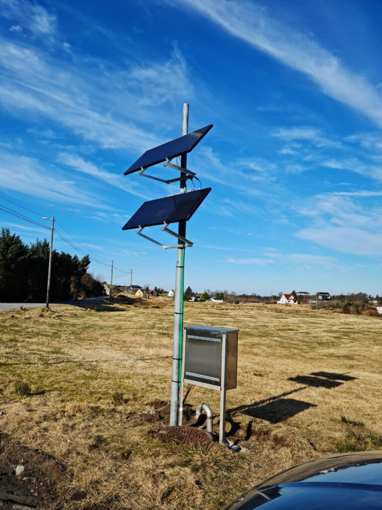 Solpaneler monterade på en stolpe i ett gräsbevuxet fält med en klarblå himmel i bakgrunden.