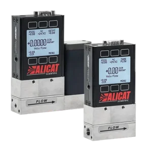 Två Alicat Scientific flödesmätare med digitala displayer visar flödesmätningar och driftinställningar. Enheterna är placerade i vinkel och ordet "FLÖDE" är märkt med pilar på metallbasen.